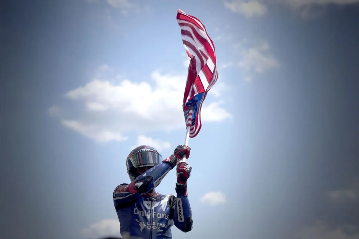 Joe Roberts con la bandera estadounidense en una imagen de archivo difundida por MotoGP en julio de 2025. No es una fotografía de la firma del contrato de 2027.